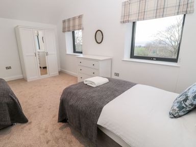 A bedroom with two beds a wardrobe a chest of drawers and two windows at Shepherds House in Lowick