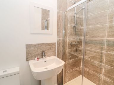 A bathroom with a white sink and mirror alongside a glass-enclosed shower with tiled walls at Shepherds House in Lowick