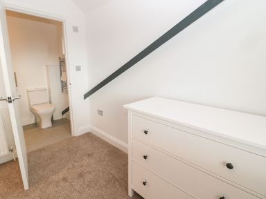 A hallway with a white dresser and an open door showing a bathroom with a toilet at Shepherds House in Lowick