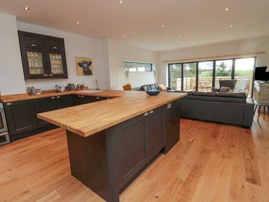 A kitchen and living room with wooden countertops a black sofa and large windows at Shepherds House in Lowick
