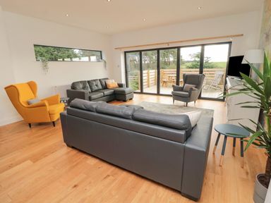 A living room with sofas chairs and a TV next to a large window overlooking a patio at Shepherds House in Lowick