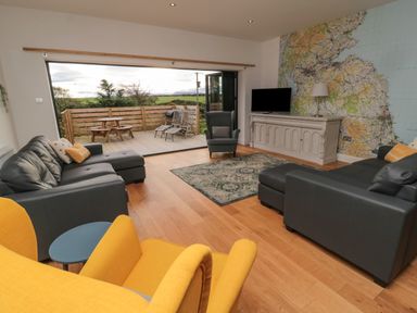 A living room with gray sofas yellow armchairs a wooden floor a map on the wall and an outdoor deck with seating at Shepherds House in Lowick