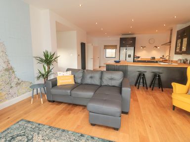 An open-plan living room and kitchen with a gray sectional sofa a yellow armchair and a kitchen island with bar stools at Shepherds House in Lowick