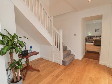 A hallway with wooden flooring, a staircase with carpeted steps, a small wooden table with items, and a potted plant at Shepherds House in Lowick