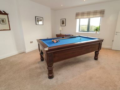 A room with a blue felt pool table wooden furniture framed pictures on the walls a window with a plaid valance and a potted plant at Shepherds House in Lowick
