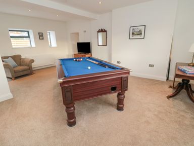 A game room with a pool table a chair a television and a table with board games at Shepherds House in Lowick