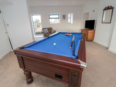 A room with a pool table with blue felt two pool cues a brown armchair a wooden cabinet with a television and a wall mirror at Shepherds House in Lowick