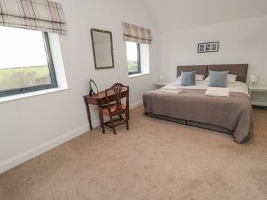 A bedroom with a double bed, two windows with striped blinds, a wooden chair and desk with a mirror at Shepherds House in Lowick