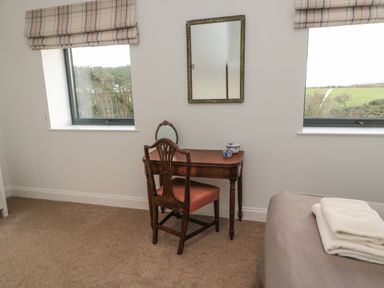 A bedroom with a wooden desk and chair between two windows and a bed with folded towels at Shepherds House in Lowick