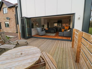 A wooden deck with a round table and chairs outside a living room with sofas at Shepherds House in Lowick