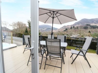 A patio with a table and six chairs under an umbrella overlooking hills at Red Kite Lodge in St Fillans