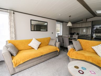 A living room with two sofas covered with yellow throws a dining table with chairs and a kitchen area at Red Kite Lodge in St Fillans
