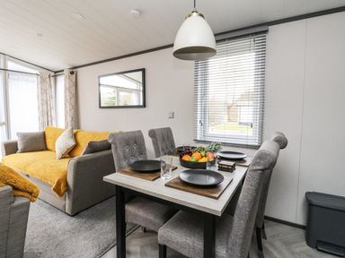A dining area with a table set for four near a window with blinds and a gray sofa with yellow throws and pillows in a living room at Red Kite Lodge in St Fillans