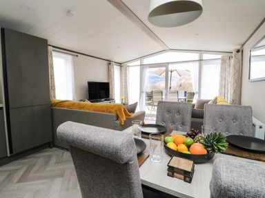A dining table with fruit bowl and plates next to a living area with sofas and a television at Red Kite Lodge in St Fillans