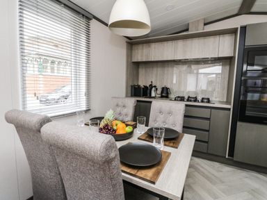 A dining table set with plates and glasses next to a kitchen with built-in appliances at Red Kite Lodge in St Fillans