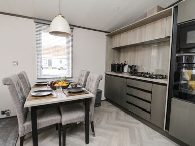 A dining table set with plates and glasses next to a kitchen area with stove and cabinets at Red Kite Lodge in St Fillans