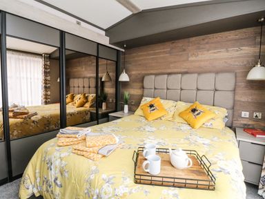 A bedroom with a bed with yellow floral bedding and bee pillows a tray with cups and teapot and mirrored wardrobes at Red Kite Lodge in St Fillans