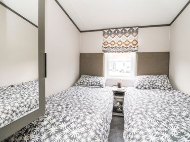A bedroom with two single beds with daisy patterned bedding and a window with a patterned blind at Red Kite Lodge in St Fillans