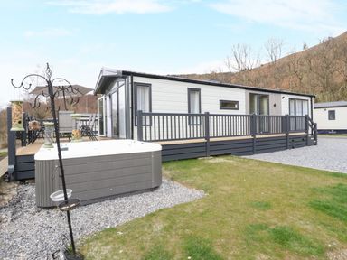 A mobile home with a deck hot tub and bird feeders on a grassy plot at Red Kite Lodge in St Fillans
