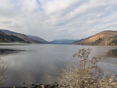 A lake surrounded by hills with a cloudy sky and bare shrubs by the shore at Red Kite Lodge in St Fillans