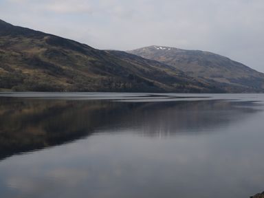 A lake with mountains in the background and reflections on the water at Red Kite Lodge in St Fillans