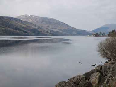 A large lake with hills in the background and rocks and shrubs in the foreground at Red Kite Lodge in St Fillans