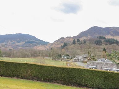 A rural landscape with sheep grazing in a field houses near trees and hills in the background at Red Kite Lodge in St Fillans