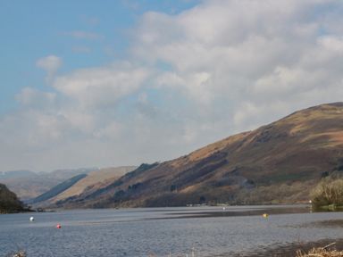 A lake with hills in the background under a partly cloudy sky at Red Kite Lodge in St Fillans