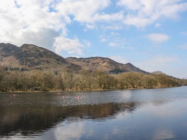 A lake with buoys and trees along the shore against hills and a blue sky at Red Kite Lodge in St Fillans