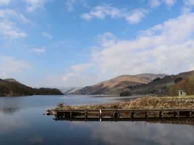 A lake with a small dock and hills in the background at Red Kite Lodge in St Fillans