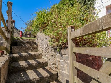 Stone steps with wooden railing leading up to a garden area with chairs and plants at Sycamore Vestry in Pontfaen near Fishguard