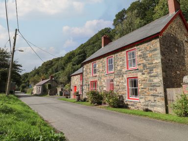 A stone house with red window frames next to a road and trees at Sycamore Vestry in Pontfaen near Fishguard