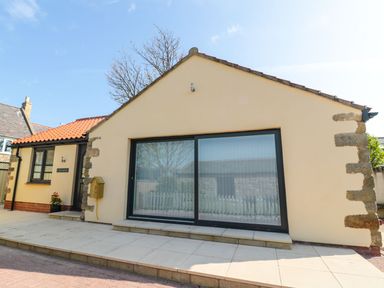 A bungalow with large sliding glass doors and a tiled roof at 3 The Paddock in Benthall near Beadnell