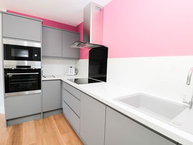 A kitchen with grey cabinets a built-in oven microwave white countertop a sink and a pink wall at 3 The Paddock Benthall near Beadnell