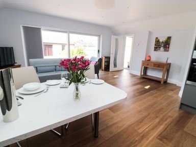 A dining area with a white table set with plates and a vase of flowers next to a living room with a blue sofa and a wooden console table at 3 The Paddock in Benthall near Beadnell