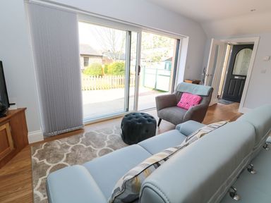 A living room with a blue sofa a gray armchair with a pink cushion a patterned rug and sliding glass doors at 3 The Paddock in Benthall near Beadnell