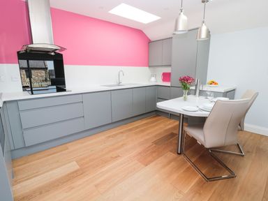 A kitchen with grey cabinets pink wall and white countertops and dining table with chairs at 3 The Paddock Benthall near Beadnell