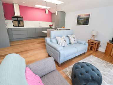 An open plan living area with a kitchen, sofas, a wooden side table, a blue ottoman and a picture on the wall at 3 The Paddock Benthall near Beadnell