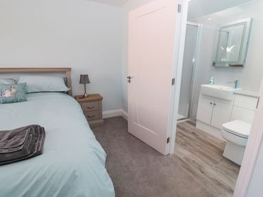 A bedroom with a bed and bedside table next to an open door leading to a bathroom at 3 The Paddock in Benthall near Beadnell