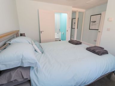 A bedroom with a bed covered in light blue bedding and two folded dark towels on the bed with a door open to a bathroom at 3 The Paddock in Benthall near Beadnell