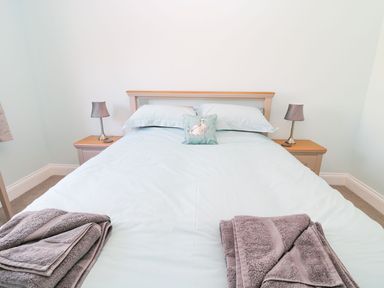 A bedroom with a double bed two bedside tables each with a lamp and folded towels on the bed at 3 The Paddock in Benthall near Beadnell