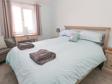 A bedroom with a bed and folded towels on it a desk and curtains by the window and a chair at 3 The Paddock in Benthall near Beadnell