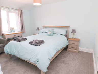A bedroom with a double bed bedside tables lamps a window with curtains and a dressing table at 3 The Paddock Benthall near Beadnell