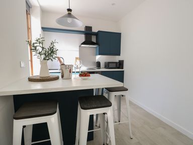 A kitchen with blue cabinets a white countertop bar stools and a flower vase at Llety Pen Deitsh 1 in Caernarfon