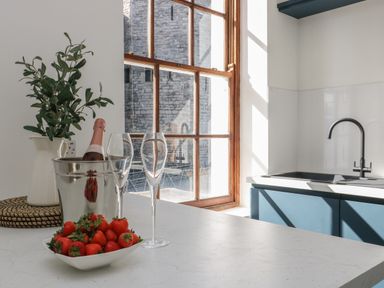 A kitchen countertop with a bowl of strawberries a bottle of wine in an ice bucket two wine glasses a vase with leaves and a sink with a faucet at Llety Pen Deitsh 1 in Caernarfon