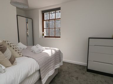 A bedroom with a bed with pillows and rolled towels a window wardrobe and a chest of drawers at Llety Pen Deitsh 1 in Caernarfon