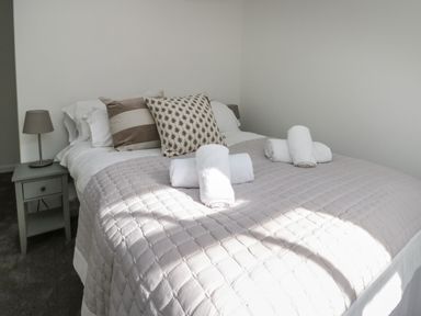 A bedroom with a bed covered in white and beige linens with pillows and rolled towels at Llety Pen Deitsh 1 in Caernarfon