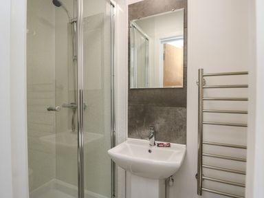 A bathroom with a glass shower enclosure a white sink a mirror and a metal towel rack at Llety Pen Deitsh 1 in Caernarfon