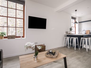 A living area with a wooden coffee table and TV mounted on the wall next to a kitchen island with stools at Llety Pen Deitsh 1 Caernarfon