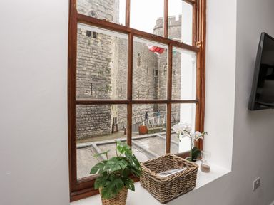 A window with plants and a wicker basket on the sill looking out to stone castle walls at Llety Pen Deitsh 1 in Caernarfon